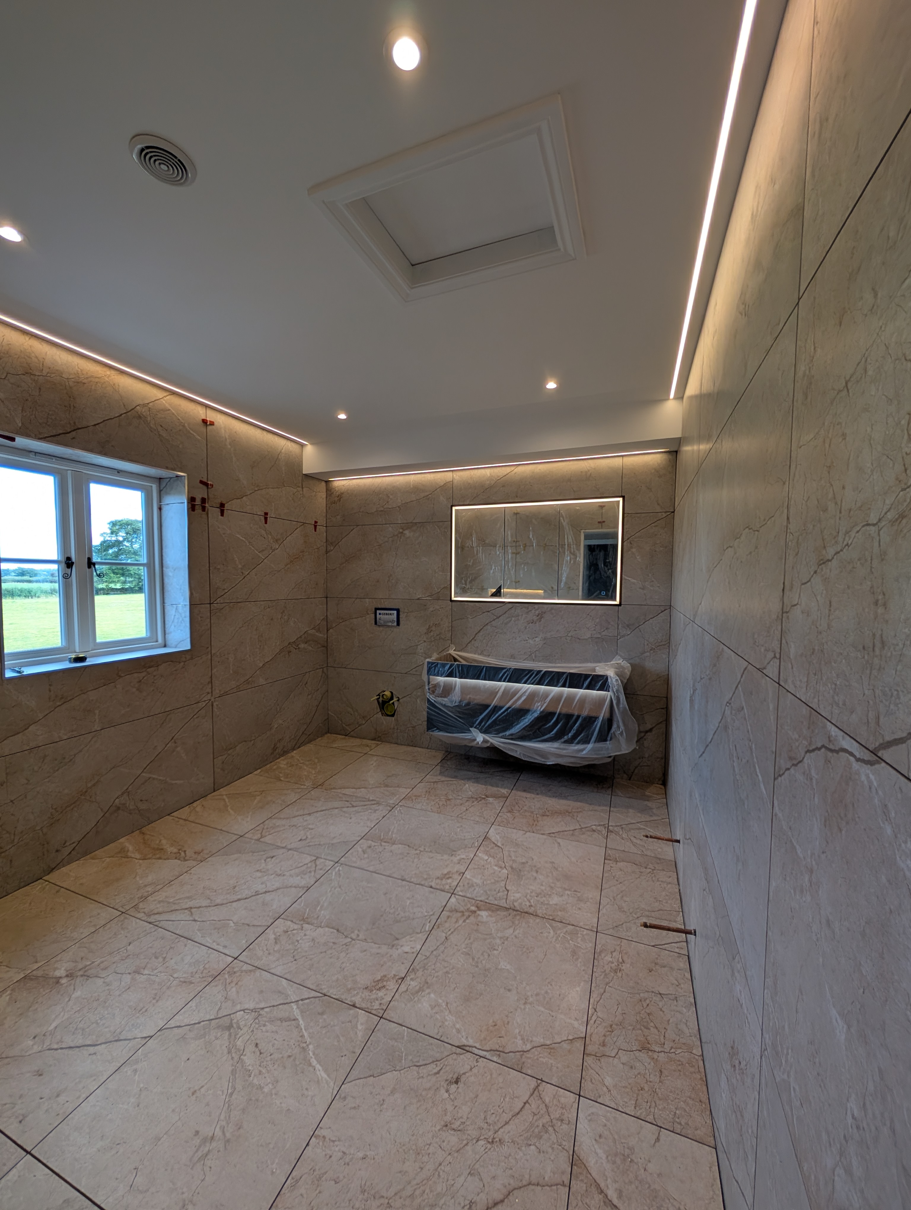 Marble-effect large-format wall and floor tiling in a rural Staffordshire bathroom with LED coving and skylight